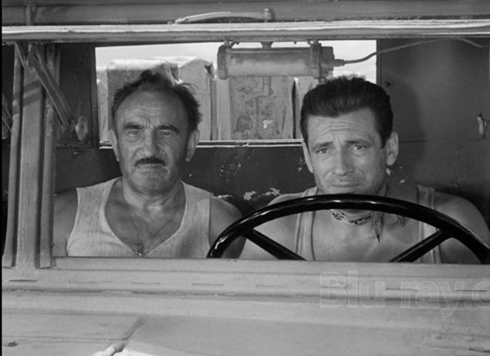 A scene from Henri-Georges Clouzot's 1953 film The Wages of Fear. Yves Montand as Mario Livi drives one of the trucks loaded with nitroglycerine. Charles Vanel as Jo is in the passenger seat.