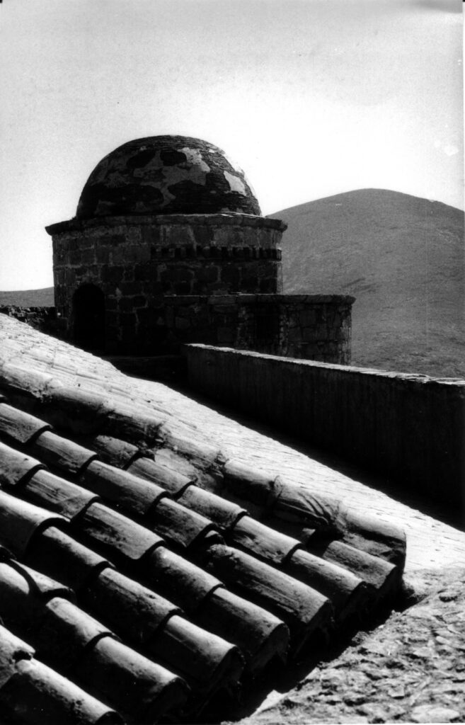 Tiled roof and domed tower of the castle at La Calahorra, Spain, against the hazy mountain landscape. Black and white photograph taken in 1982