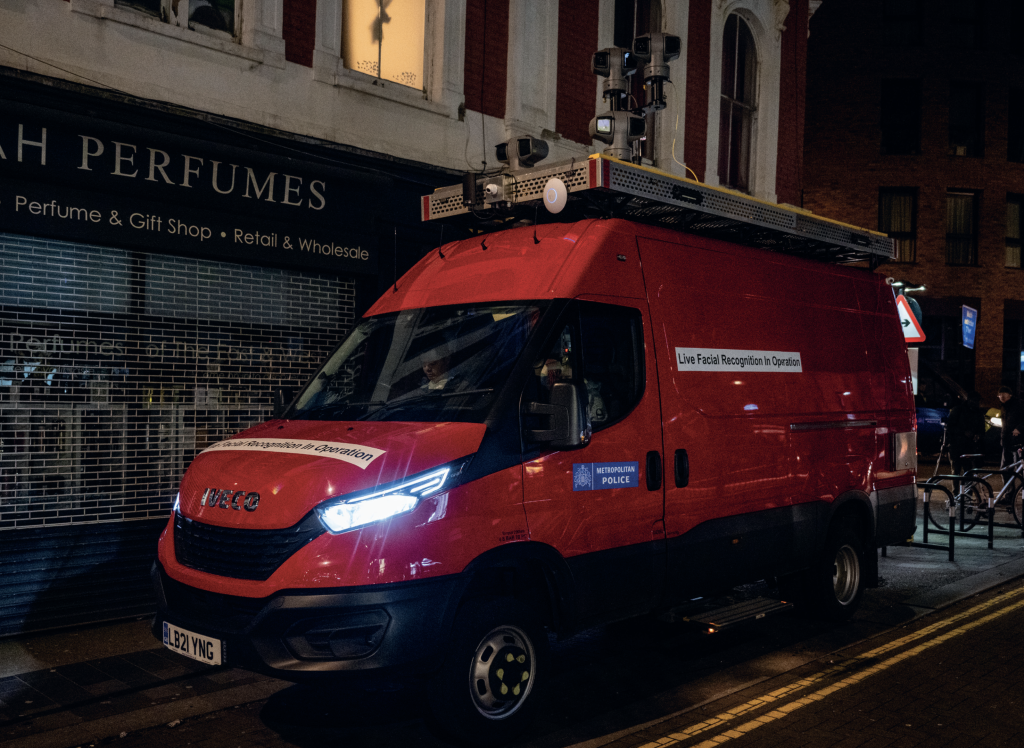 A red Metropolitan Police panel van with an array of cameras on the roof and a sign on the side that reads: 'live facial recognition in operation'